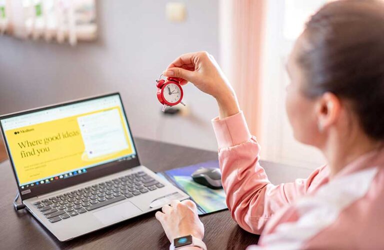 Woman using time management tools while holding a mini clock at desk