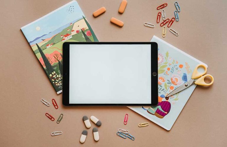 Tablet on a desk surrounded by paper clips, notebooks, and stationery, representing productivity tools in a creative workspace